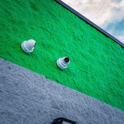 Wall-mounted commercial security cameras installed on a green and gray exterior facade