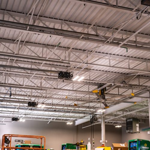 Ceiling view of industrial facility with conduit, lighting, and overhead mechanical systems.